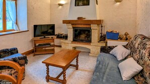 A cozy living room with a fireplace, wooden beams, a television, and a sofa. - Charming stone house in the heart of the Vosges (Saint-Bresson)