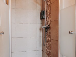 A shower area with a tiled wall, a showerhead, and a control panel.