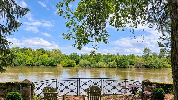 A riverside patio with a metal railing, two Adirondack chairs, a small table, and a bench. - Cozy Cottage by the Saône (Mantoche)