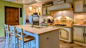 A kitchen with a central island, bar stools, a stove, and a sink. - Cozy Cottage by the Saône (Mantoche)