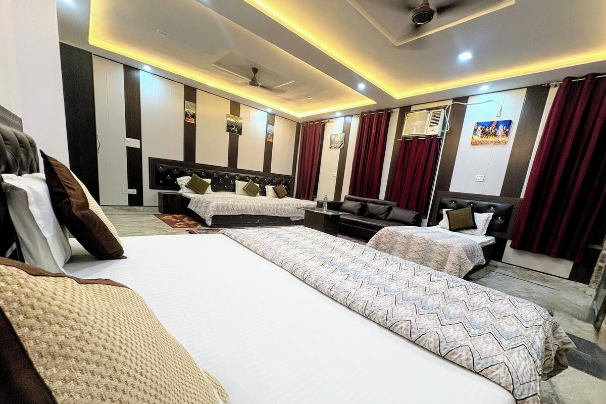 A hotel room with two beds, a sofa, a TV, and a ceiling fan.