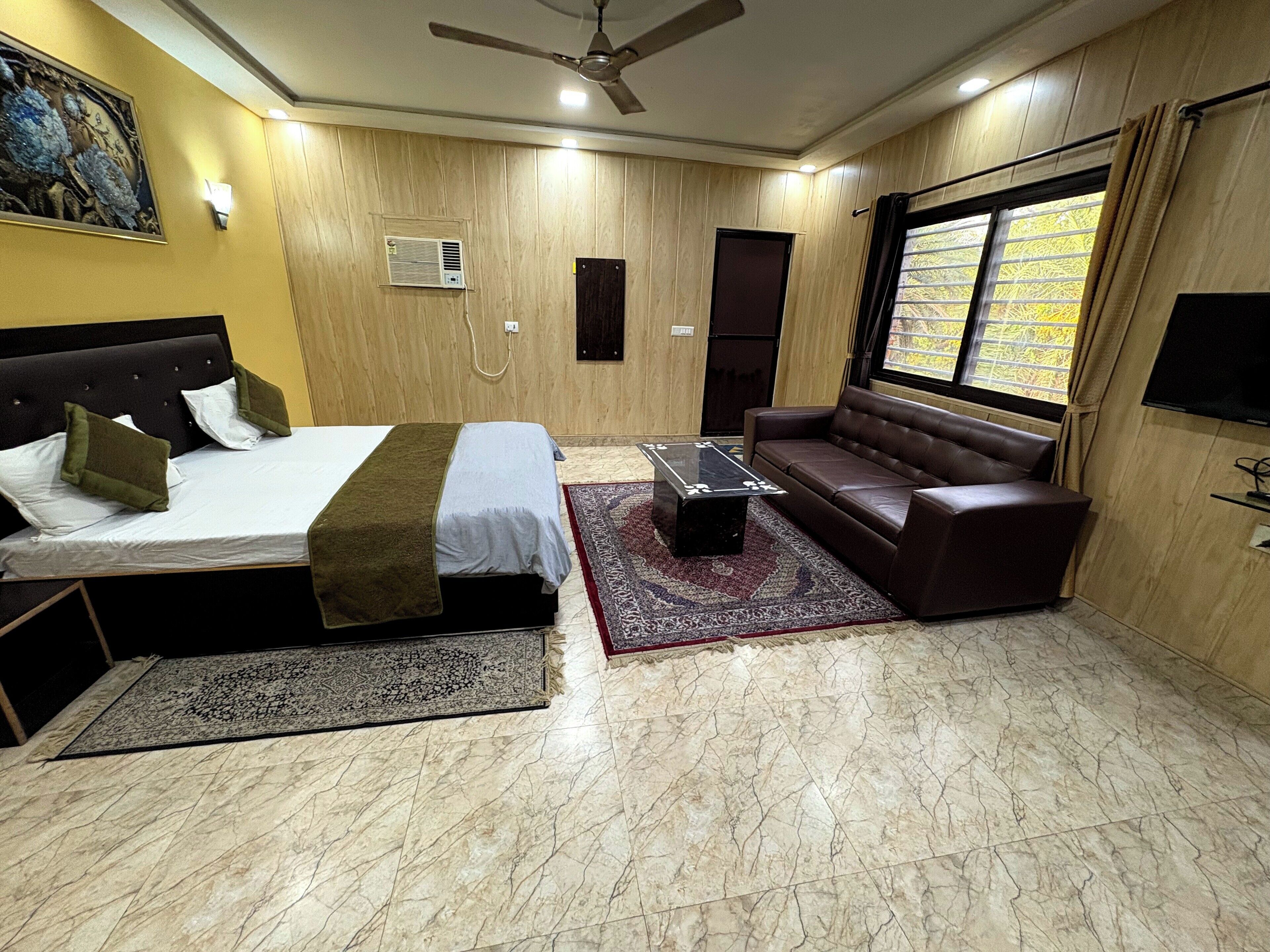 A bedroom with a bed, a sofa, a coffee table, a TV, and a window with curtains.