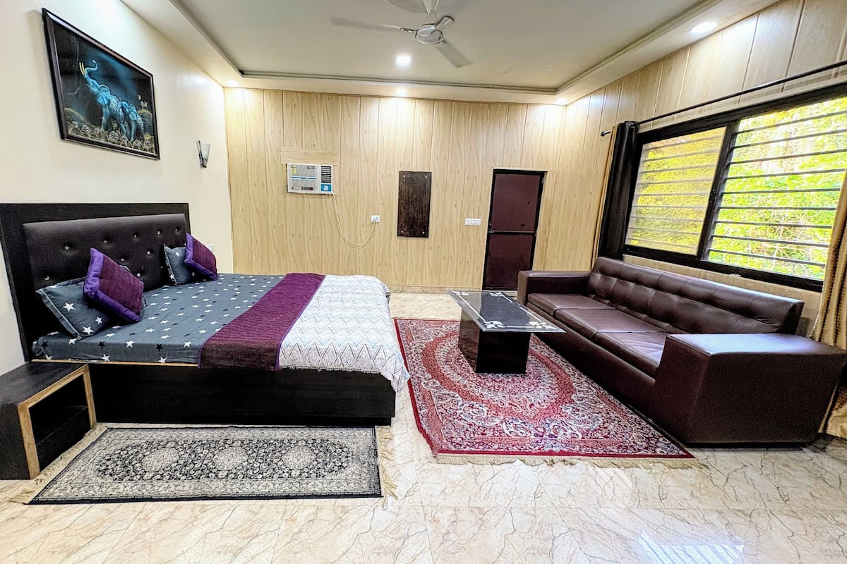 A bedroom with a bed, a sofa, a coffee table, a window with a view, and a ceiling fan.