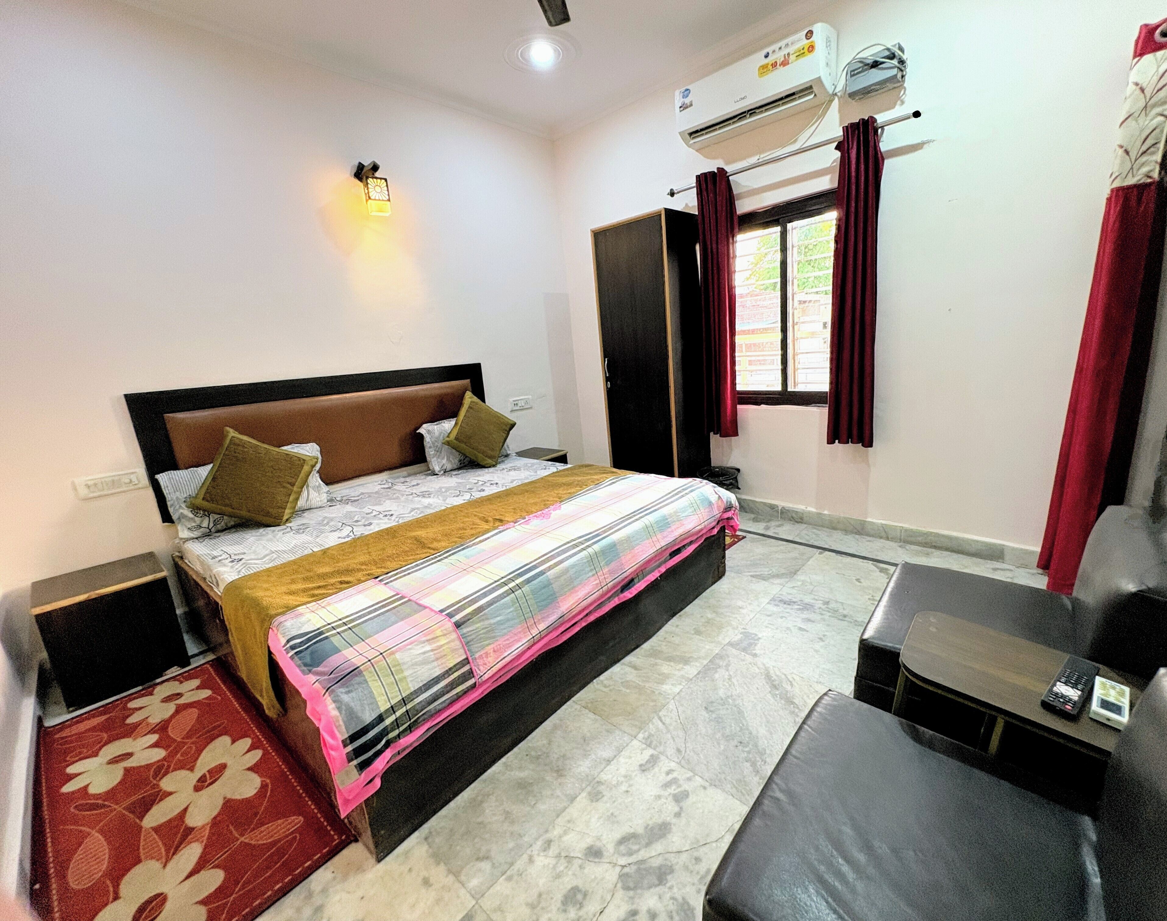 A bedroom with a bed, a desk, an air conditioner, and a window with curtains.