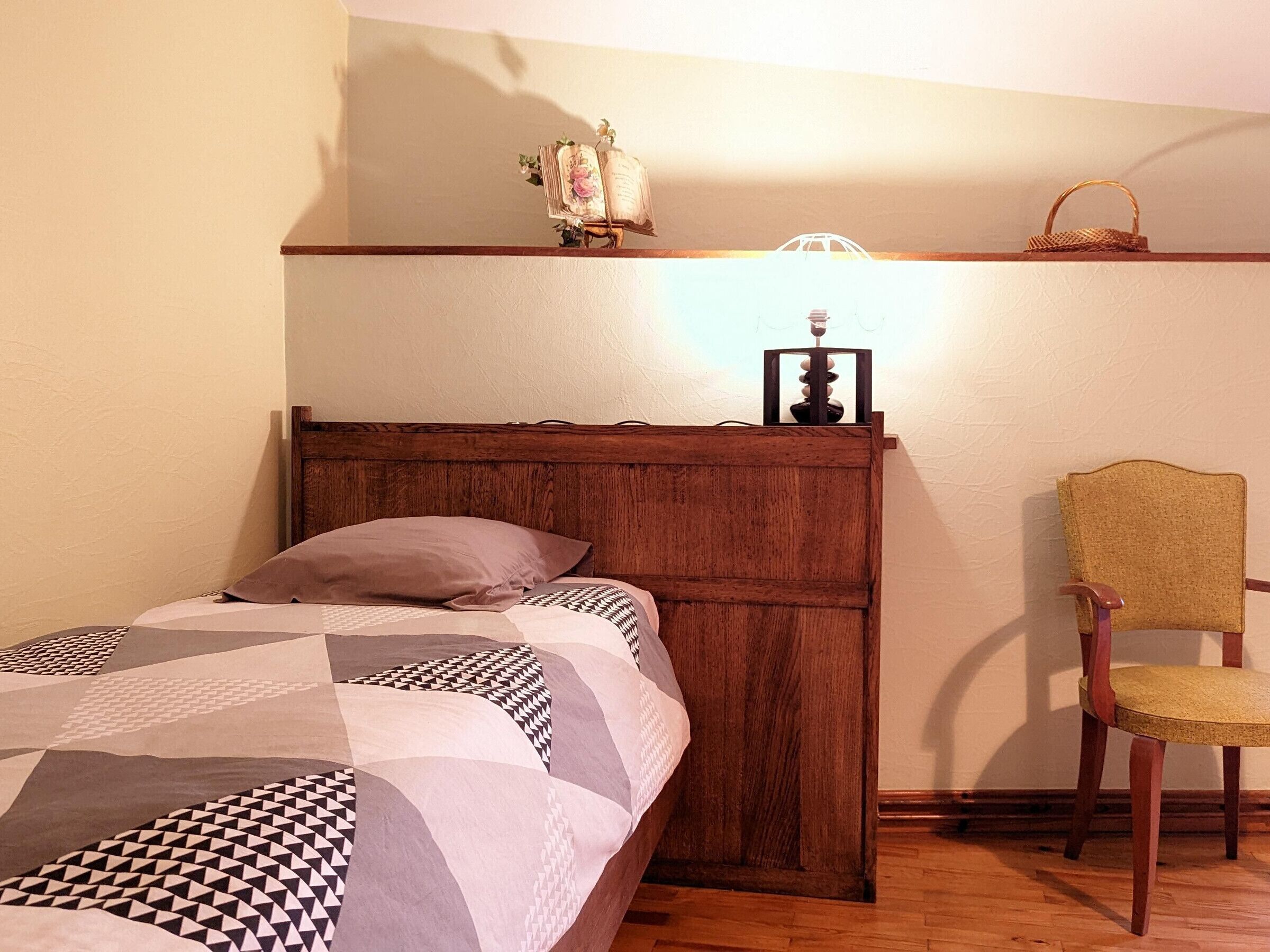 Un dormitorio con cabecera de madera, una cama con ropa de cama estampada, una silla y una estantería con adornos.