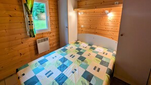 Une pièce aux murs lambrissés, avec un lit, une fenêtre et une porte.