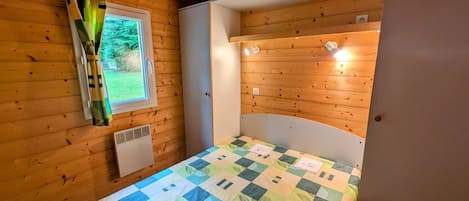 Ein Zimmer mit Holzwänden, einem Bett, einem Fenster und einer Tür.