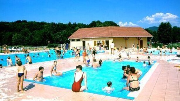 Un espace piscine comprenant plusieurs bassins, un espace de repos couvert et un bâtiment en arrière-plan.