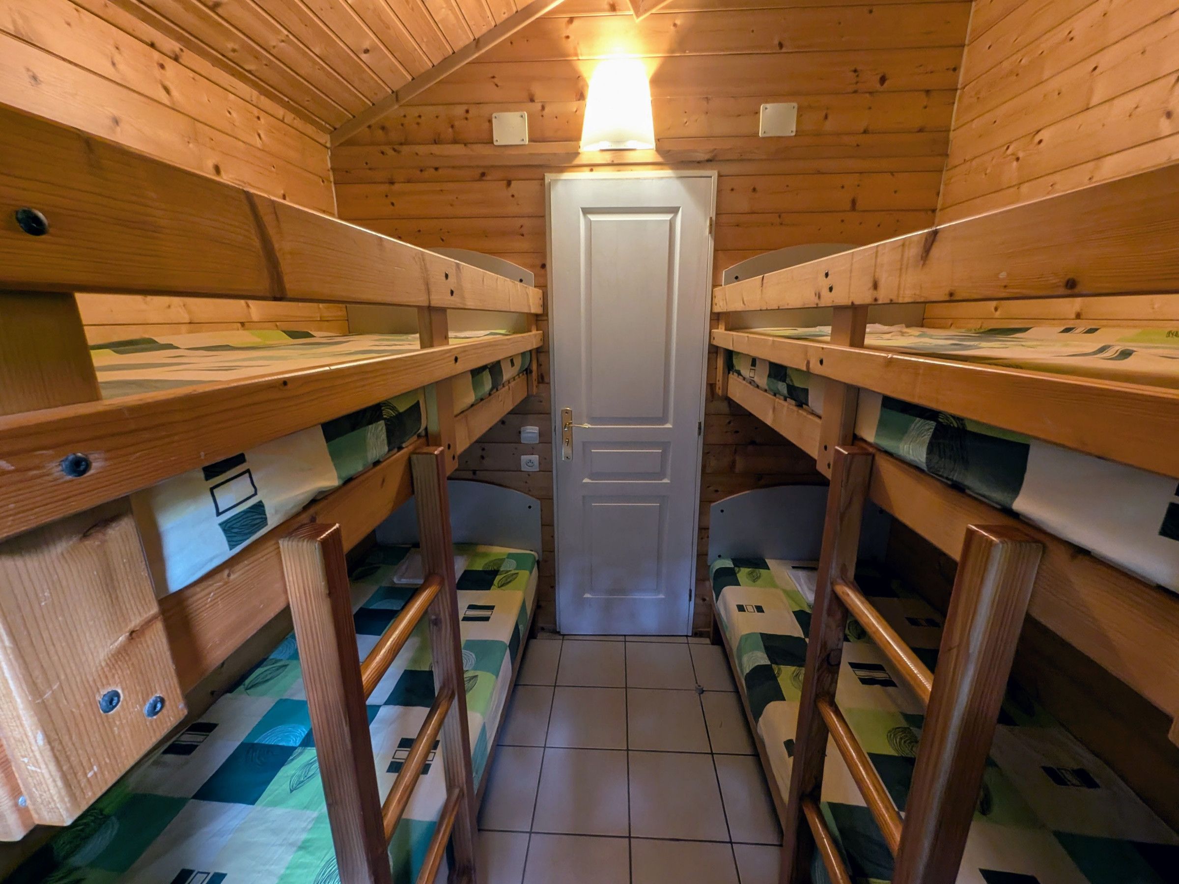 A cabin with wooden walls, a central door, and bunk beds with patterned bedding.
