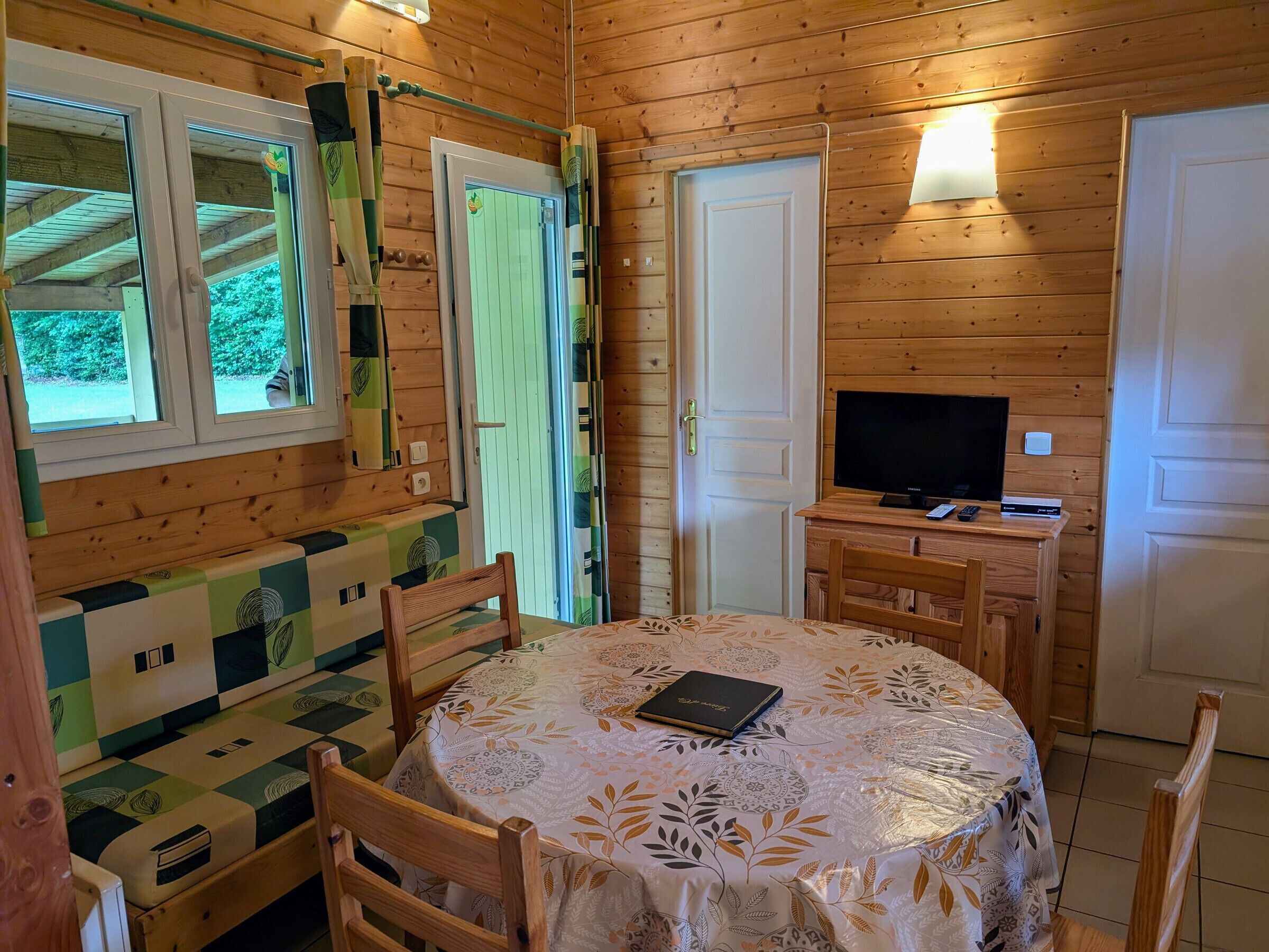 Un intérieur en bois avec une table ronde, des chaises, un téléviseur et un mur orné de motifs.
