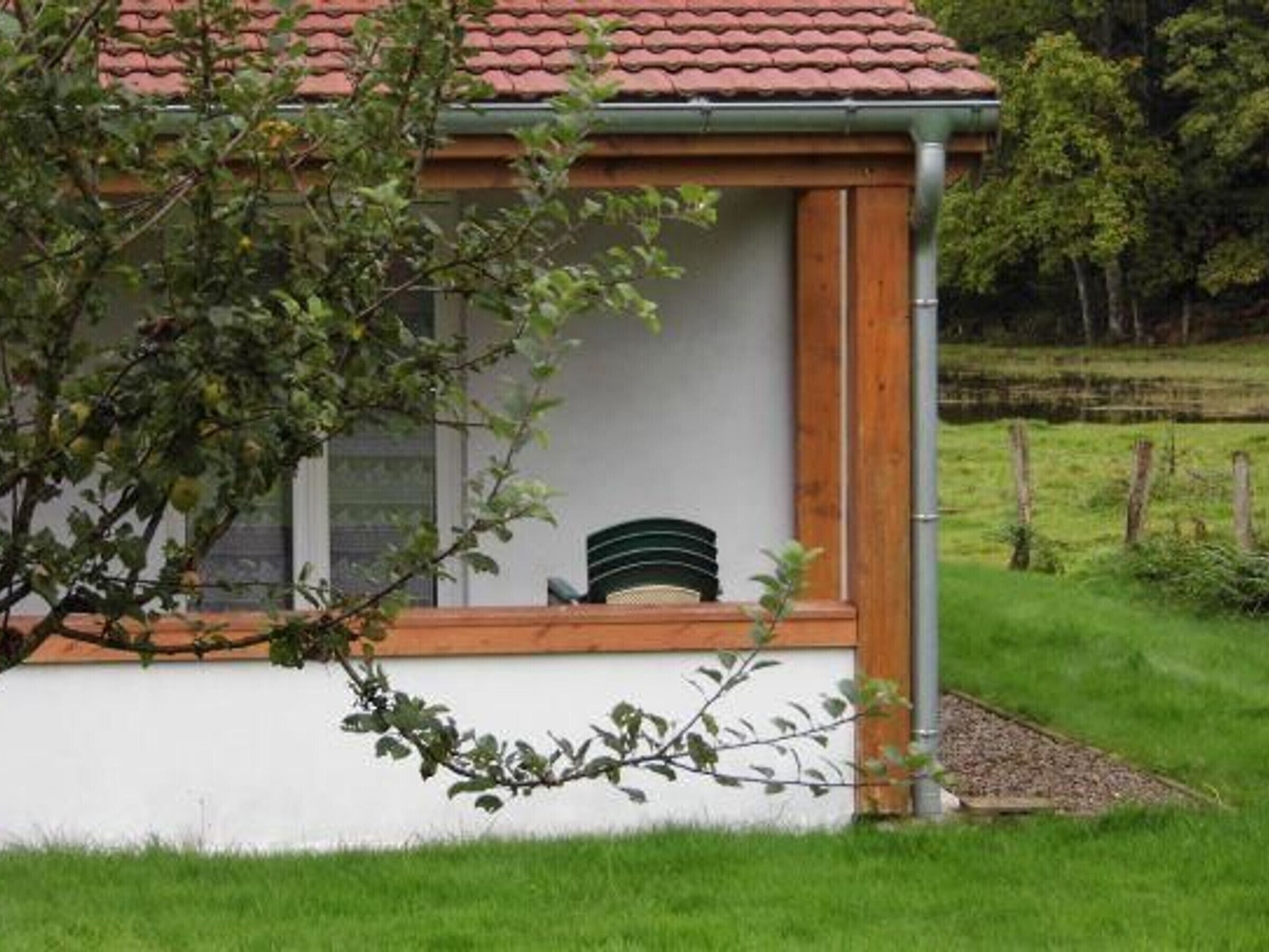 A small, single-story building with a red-tiled roof, a wooden porch, and a white exterior wall.