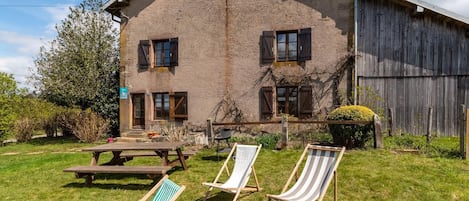 A rustic building with a wooden exterior, a picnic table, and two lounge chairs in a grassy yard.