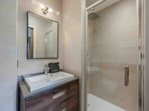 A modern bathroom with a large mirror, a white sink, a dark wooden vanity, and a glass shower enclosure.