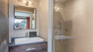 Un bagno moderno con doccia vetrata, uno specchio grande e un mobile lavabo con lavandino e cassetti.