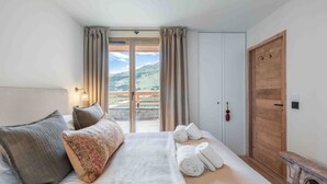 Una camera da letto con un letto, una porta in legno e vista su un paesaggio montuoso attraverso una porta scorrevole.