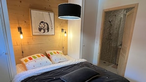 A bedroom with a wooden headboard, a bed with a black comforter and pillows, a wall-mounted light, and a framed picture.