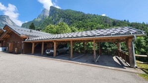 A wooden building with a covered parking area and a mountain backdrop.
