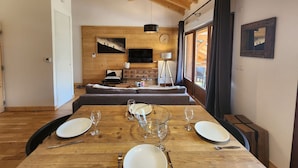 A dining area with a wooden table set for four, a sofa, and a television mounted on a wooden wall.