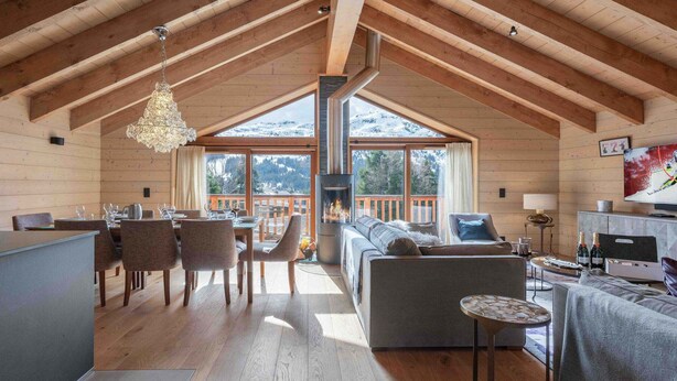 A spacious living area with a high ceiling, wooden beams, a fireplace, and a large window overlooking a snowy mountain. - Cozy chalet in Méribel with jacuzzi, sauna, 4 bedrooms (Méribel)