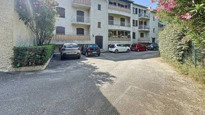 Un immeuble résidentiel à plusieurs étages, doté de balcons, d’une allée en gravier et de voitures garées.