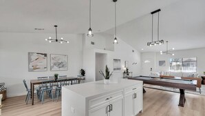 A modern kitchen with a central island, pendant lighting, and a dining area with chairs and a table.
