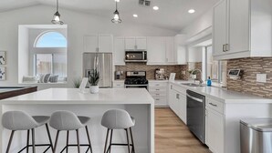 A modern kitchen with white cabinetry, a large island with bar stools, a built-in oven, and a microwave.