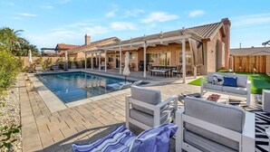 A backyard with a swimming pool, outdoor furniture, and a pergola.