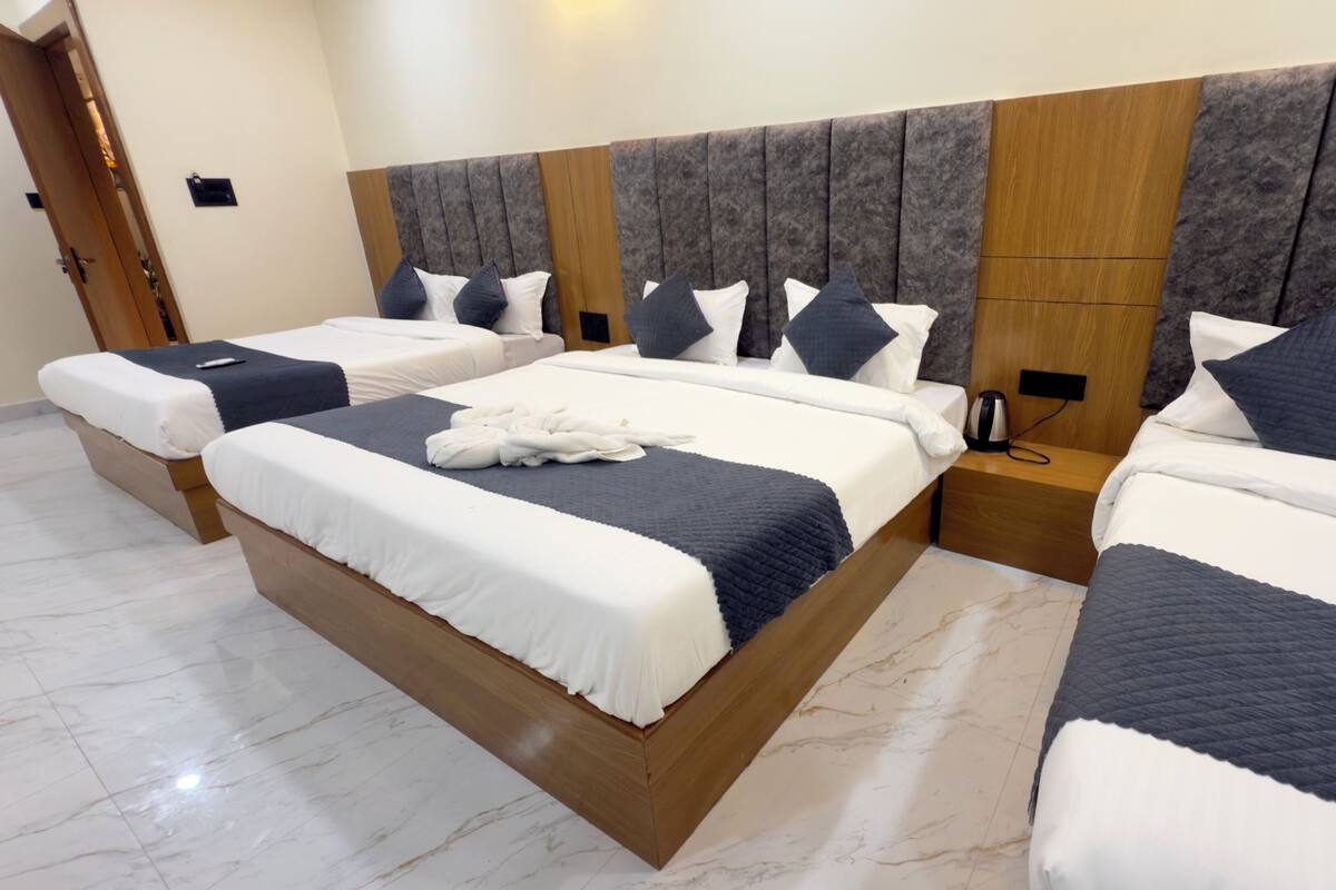 A hotel room with three beds, each with a wooden headboard and grey upholstered headboard.