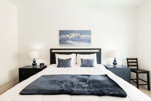 Une chambre à coucher bien rangée, avec un lit, deux tables de chevet dotées de lampes, une chaise et un tableau accroché au mur.