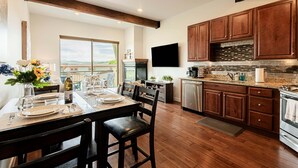 Una cocina moderna con armarios de madera, un comedor con una mesa lista para dos personas, y un ventanal con vistas panorámicas.