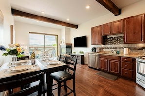 Une cuisine moderne avec des meubles en bois, un coin repas avec une table dressée pour deux personnes, et une grande fenêtre donnant sur un paysage magnifique.