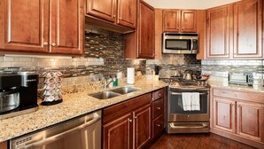Una cocina con armarios de madera, lavavajillas de acero inoxidable, microondas, estufa y fregadero.