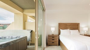 Habitación de hotel con cama de madera, dos mesitas de noche con lámparas, cabina de ducha de vidrio y bañera de hidromasaje.