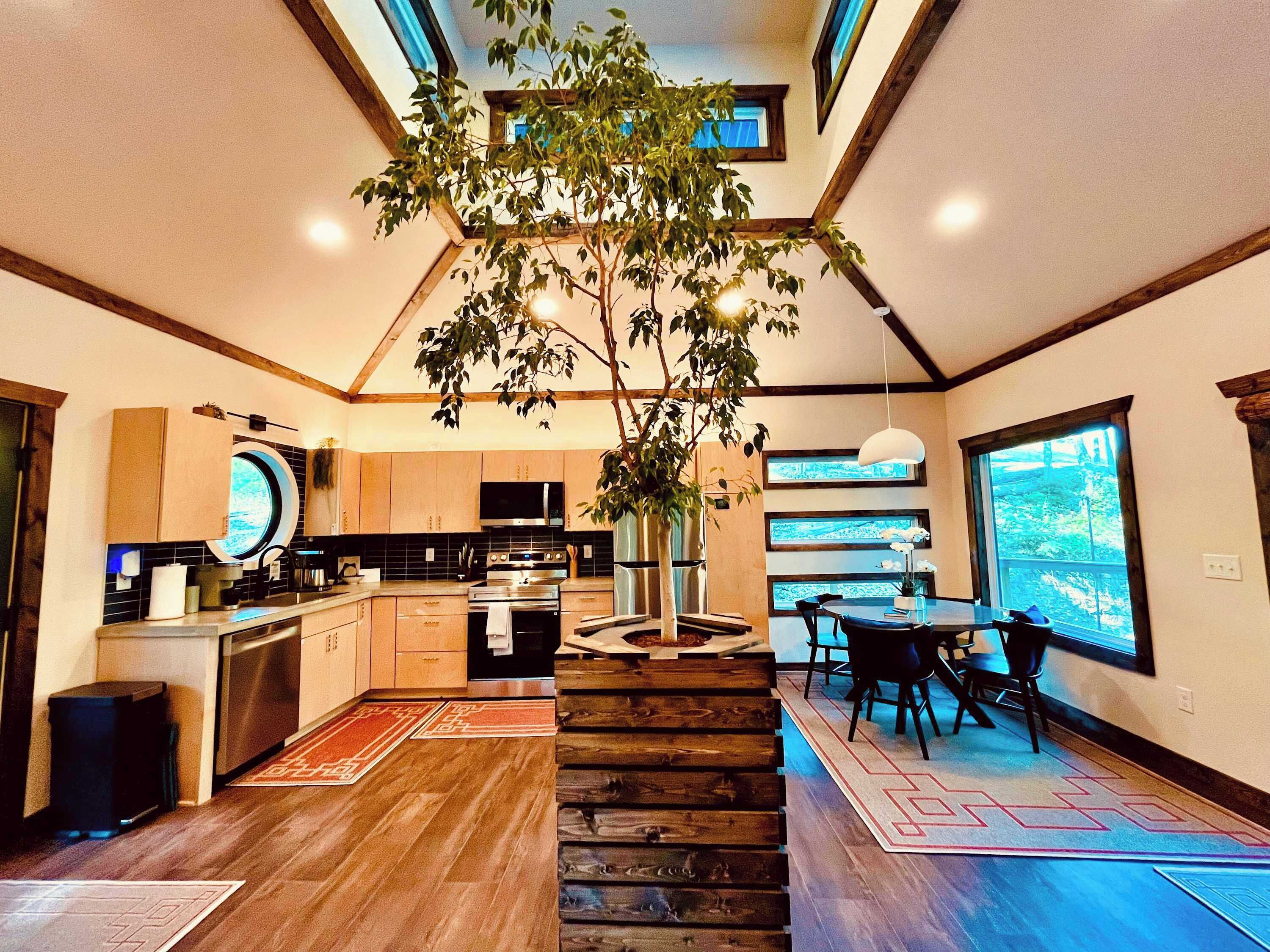 Una cocina moderna con una isla central, un comedor con un ventanal grande y una escalera que sube a un nivel superior.