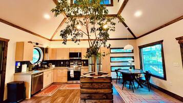 Una cocina moderna con una isla central, un comedor con un ventanal grande y una escalera que sube a un nivel superior.