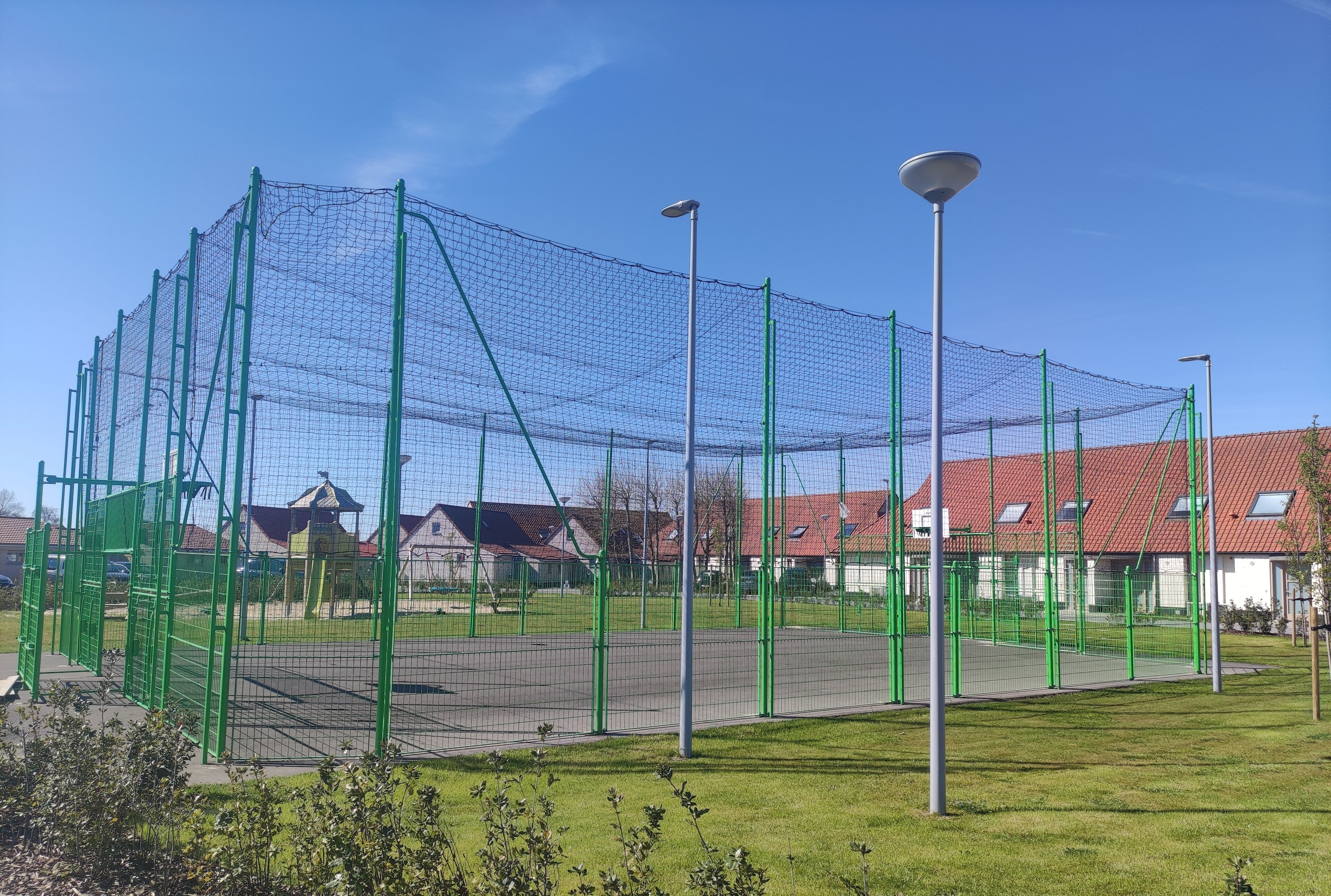 A sports facility with a netted area, green fencing, and a street lamp.