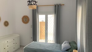 Een slaapkamer met een bed, nachtkastje, hanglamp en raam met gordijnen.