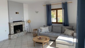 Een woonkamer met een open haard, een bank, een ronde salontafel en een vloerlamp.