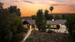 A two-story house with a tiled roof, surrounded by trees and a clear sky at sunset.
