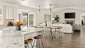 A spacious kitchen with a large island, white cabinetry, and a dining area with white chairs.