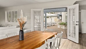 A spacious dining area with a wooden table and white chairs, leading to an outdoor patio with umbrellas and seating.