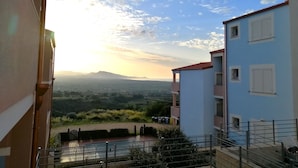Un edificio residencial con balcón que ofrece vistas a un paisaje pintoresco, incluyendo colinas a lo lejos y un cielo despejado.