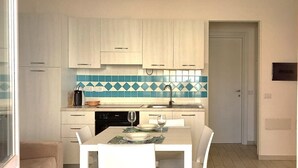 Una cocina compacta con armarios blancos, salpicadero de azulejos y un área de comedor con una mesa preparada para dos personas.