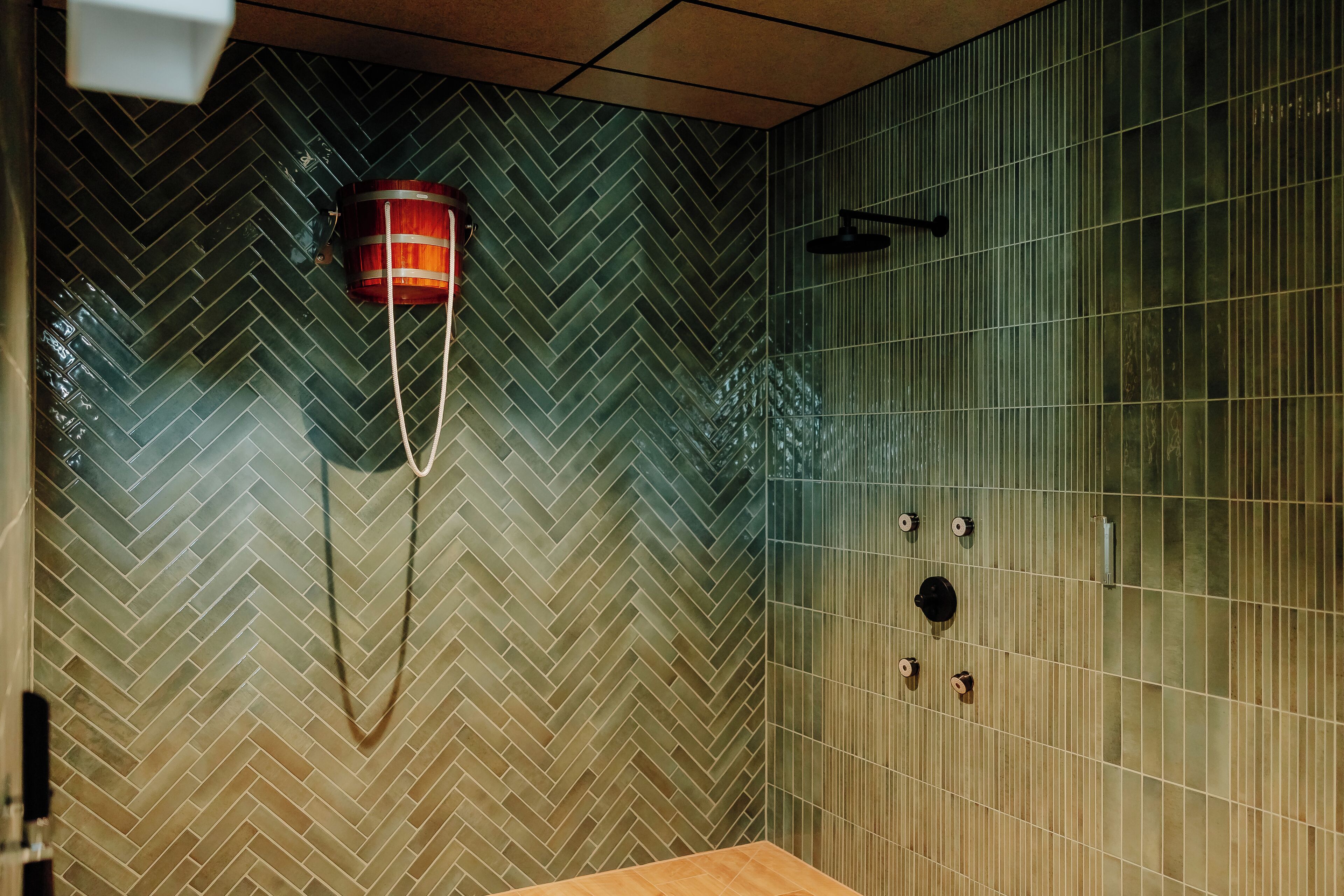 Un baño con patrón de baldosas en espiga, un banco de madera y zona de ducha con puerta de vidrio.