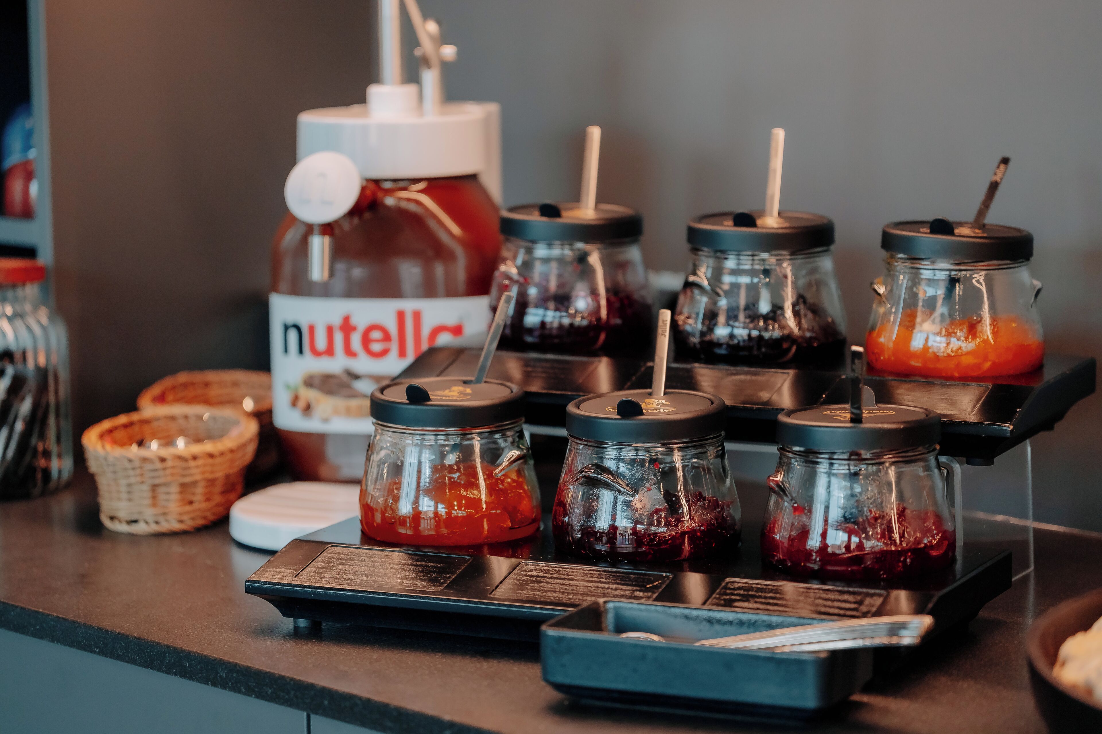 Una barra con frascos de mermelada y un dispensador de Nutella.