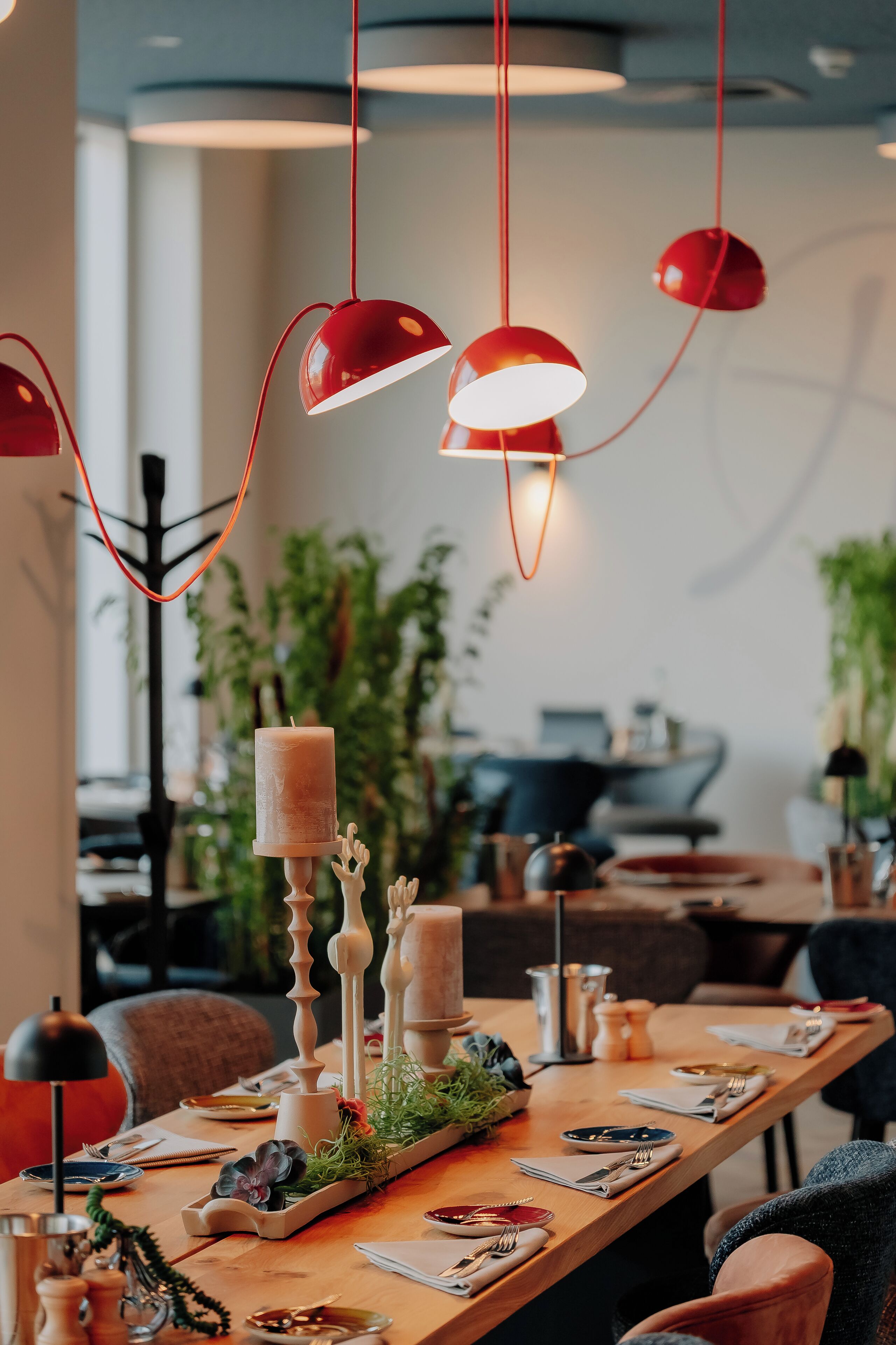 A dining area with a long table set for a meal, red pendant lights, and a candle centerpiece.