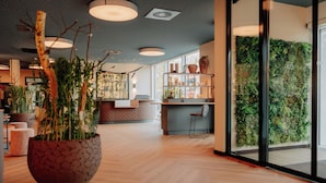 Un interior modern amb un terra de fusta, una planta gran en test i una paret verda amb plantes.