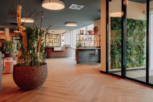 Un interior moderno con suelo de madera, una planta grande en maceta y una pared verde con plantas.