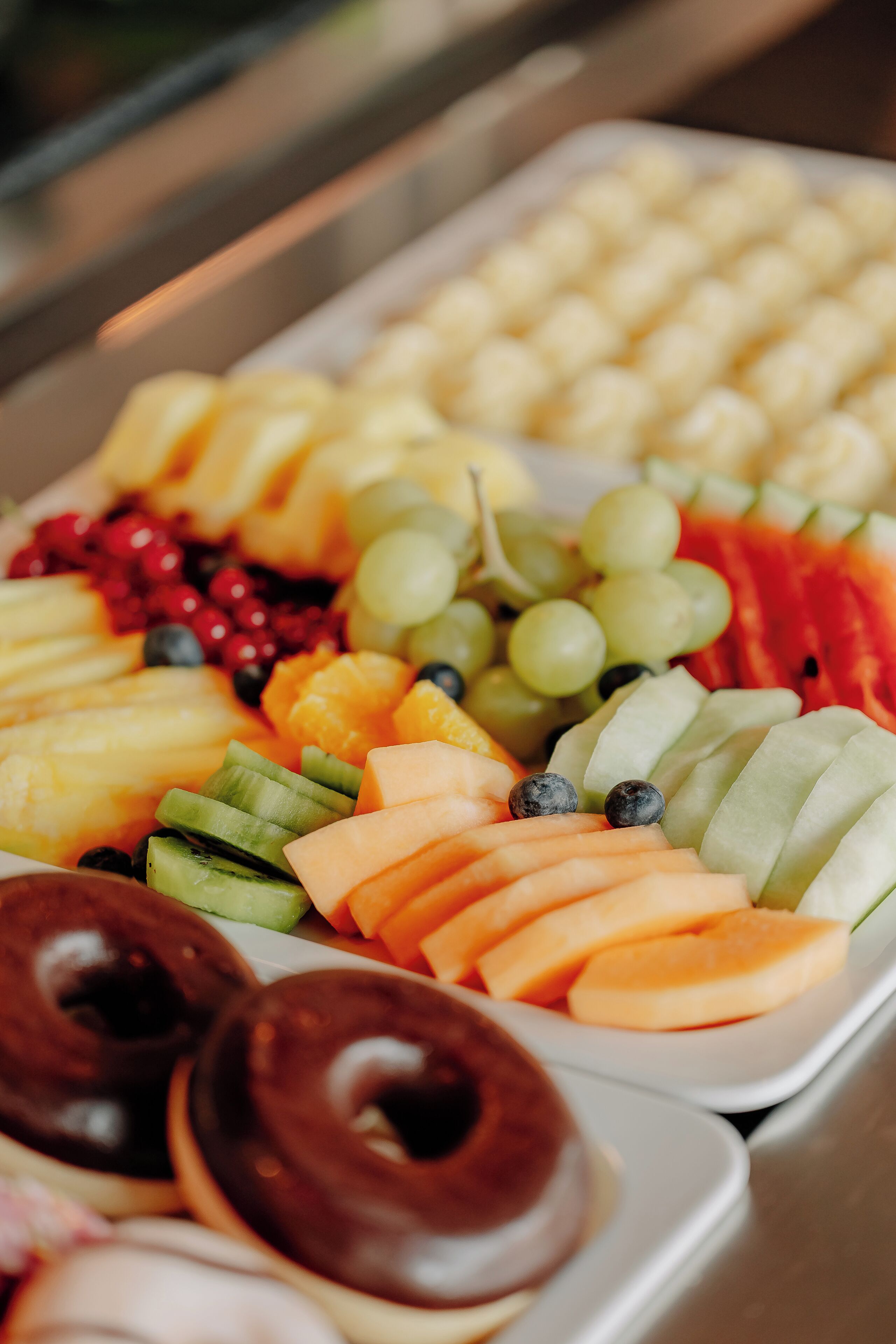 A tray of assorted fruits and chocolate donuts.