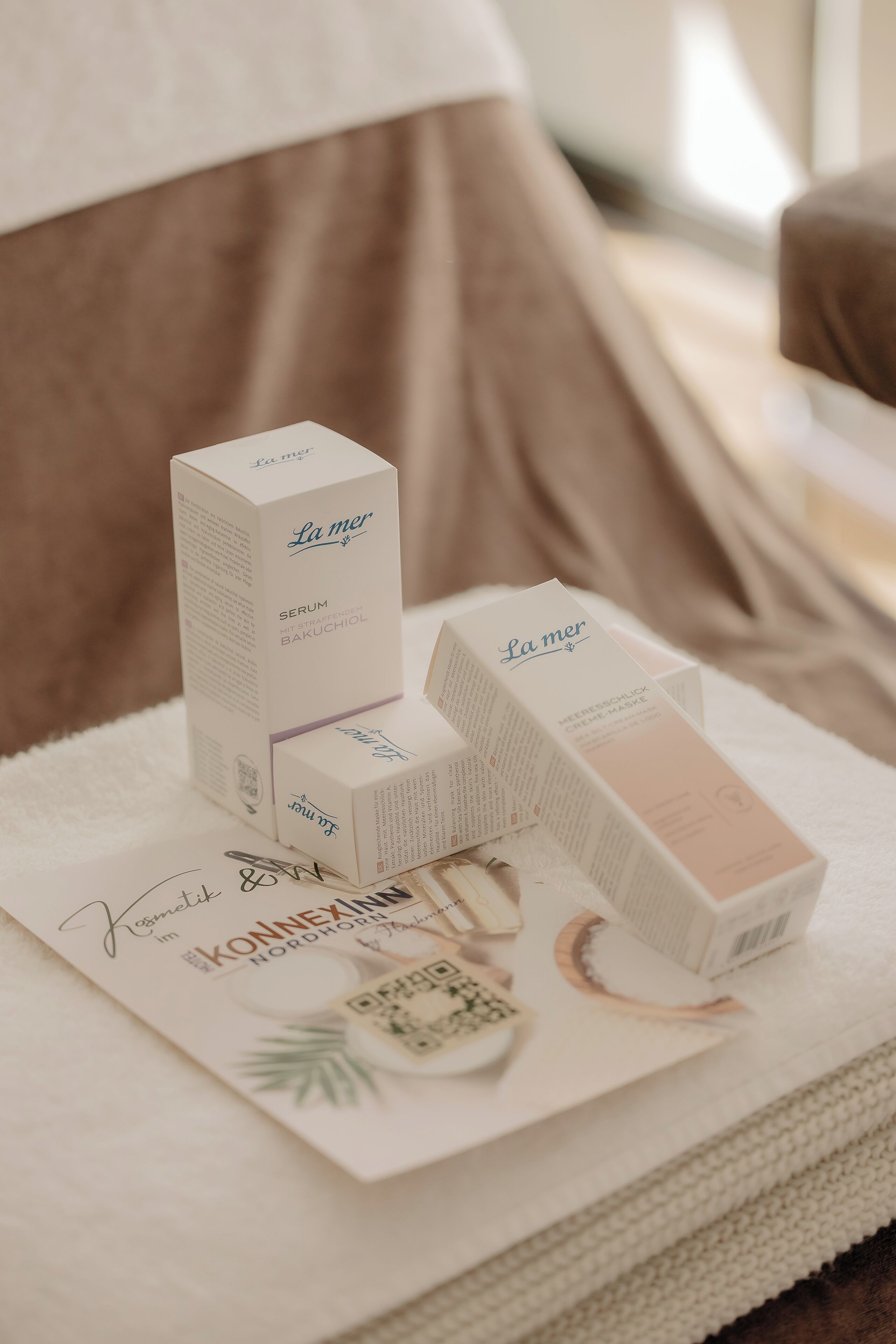 Mehrere La Mer Serum-Verpackungen auf einem weißen Handtuch, zusammen mit einem Zertifikat und einer kleinen Pflanze.